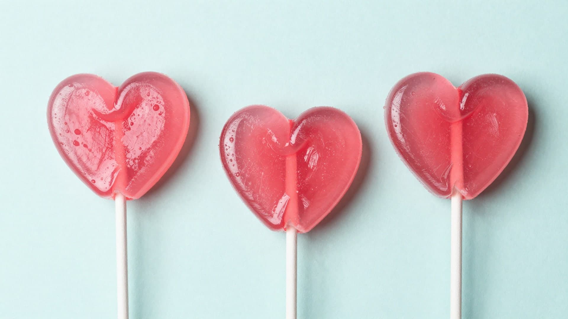 Pink heart-shaped lollipop candies arranged on pastel background.